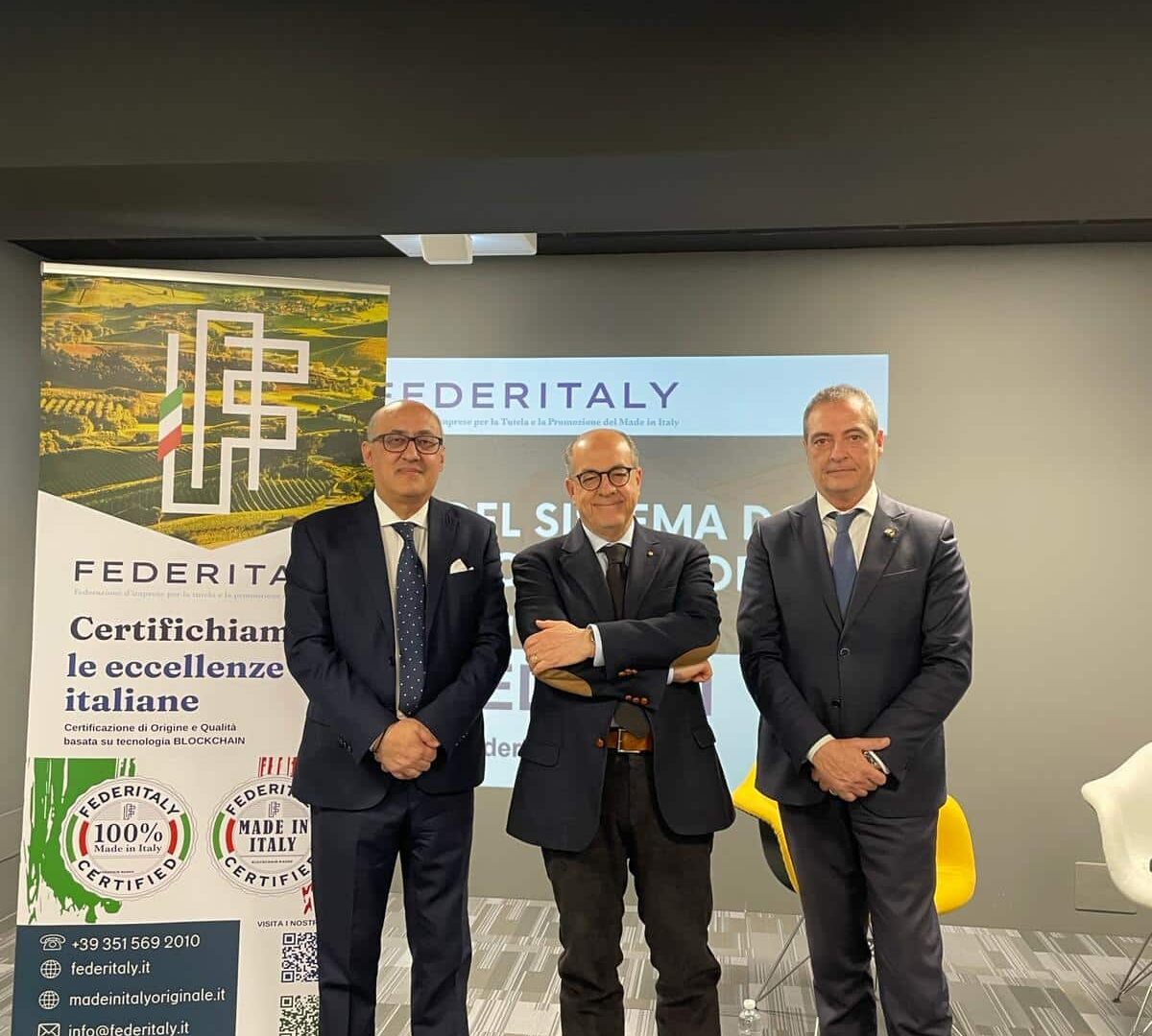 Trio di uomini in abito davanti a banner FEDITALY.