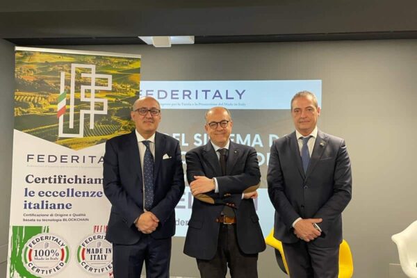 Trio di uomini in abito davanti a banner FEDITALY.
