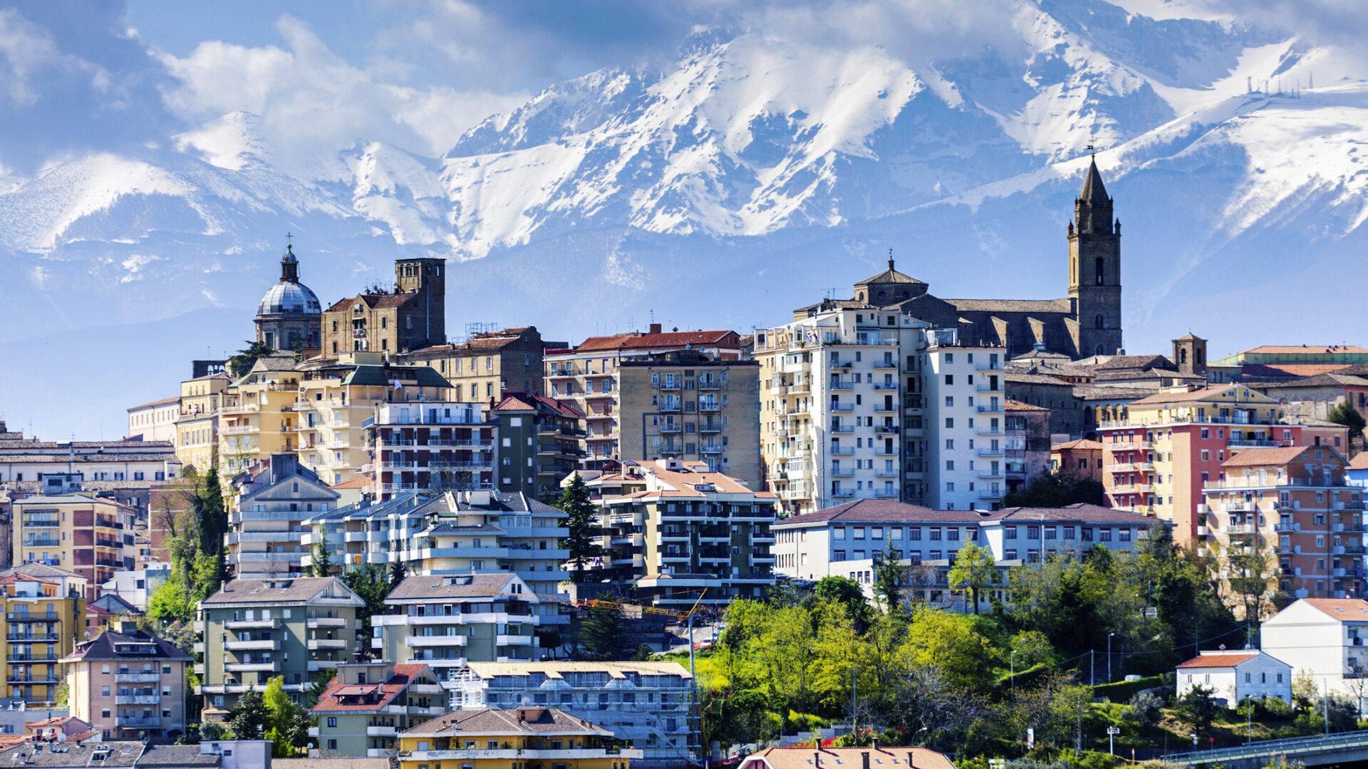 Città italiana con montagne innevate sullo sfondo.
