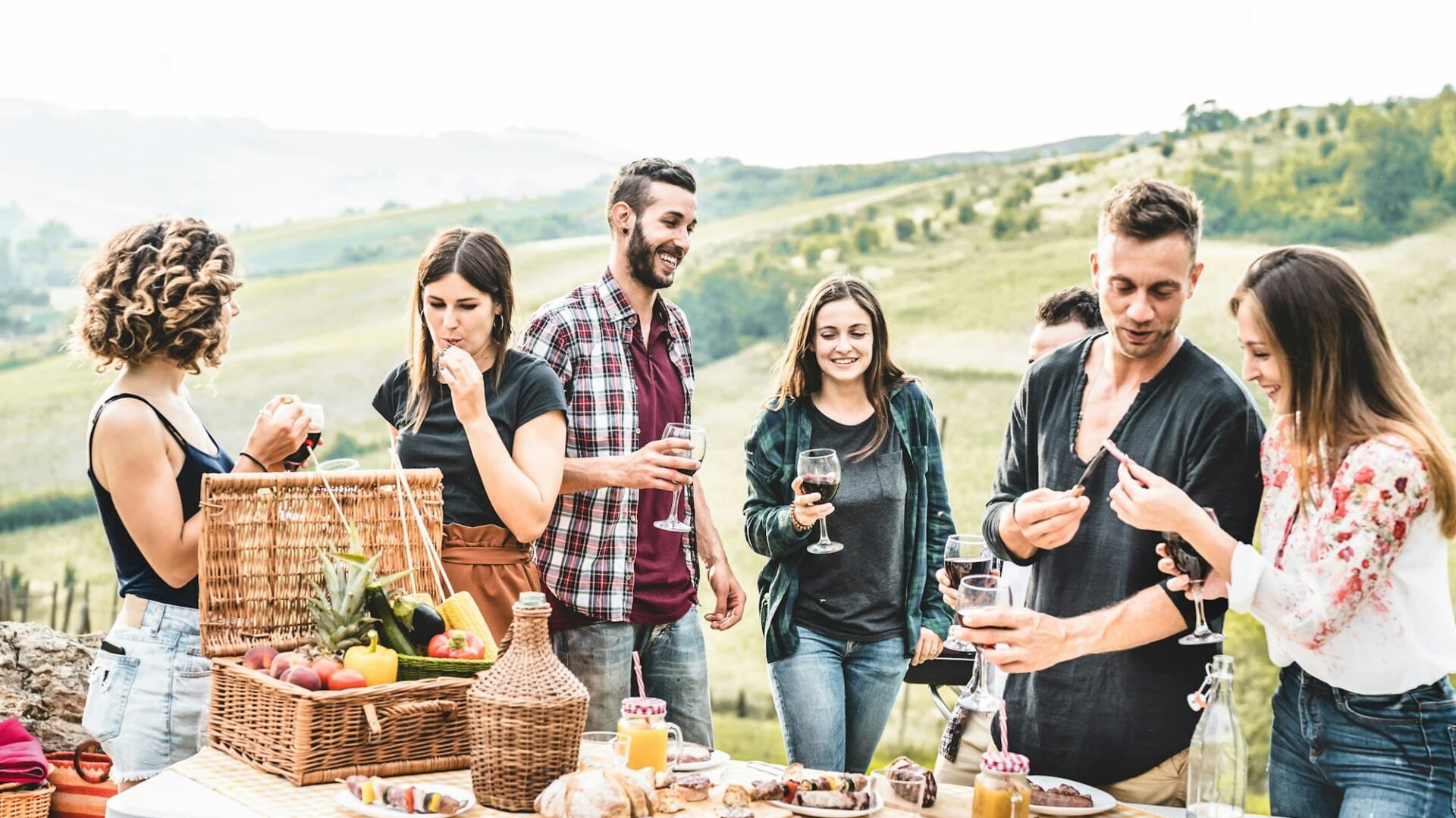 Happy adult friends eating at picnic lunch in italian vineyard outdoor