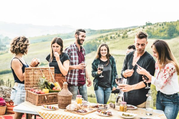 Happy adult friends eating at picnic lunch in italian vineyard outdoor