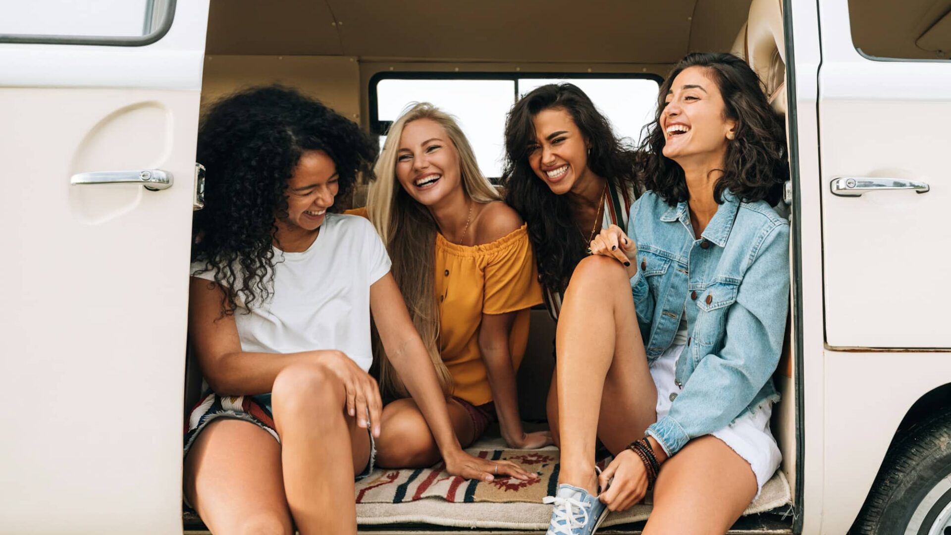 Multi ethnic group of women having fun while sitting in a car. Four friends traveling by car.