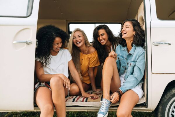 Multi ethnic group of women having fun while sitting in a car. Four friends traveling by car.