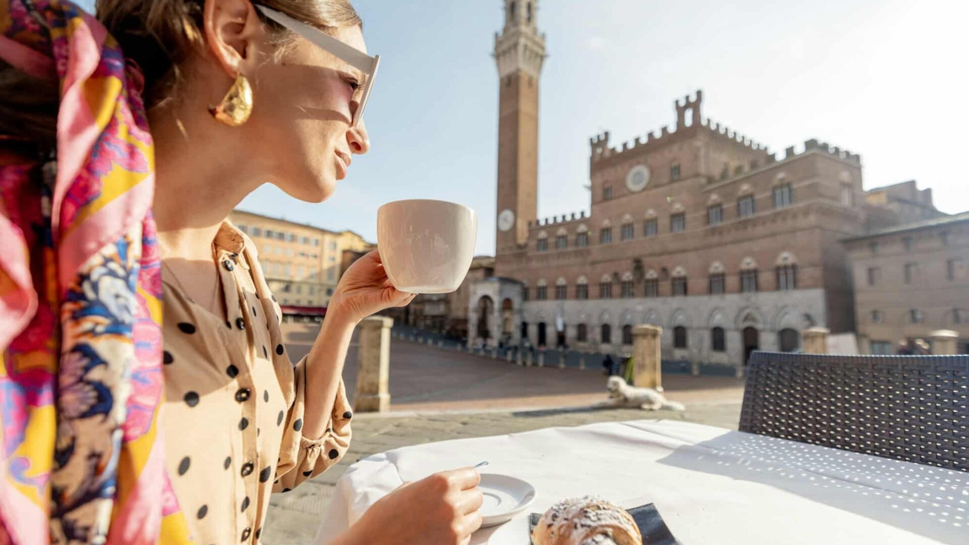 Woman having breakfast at outdoor cafe with beautiful view on main square of Siena city, Italy