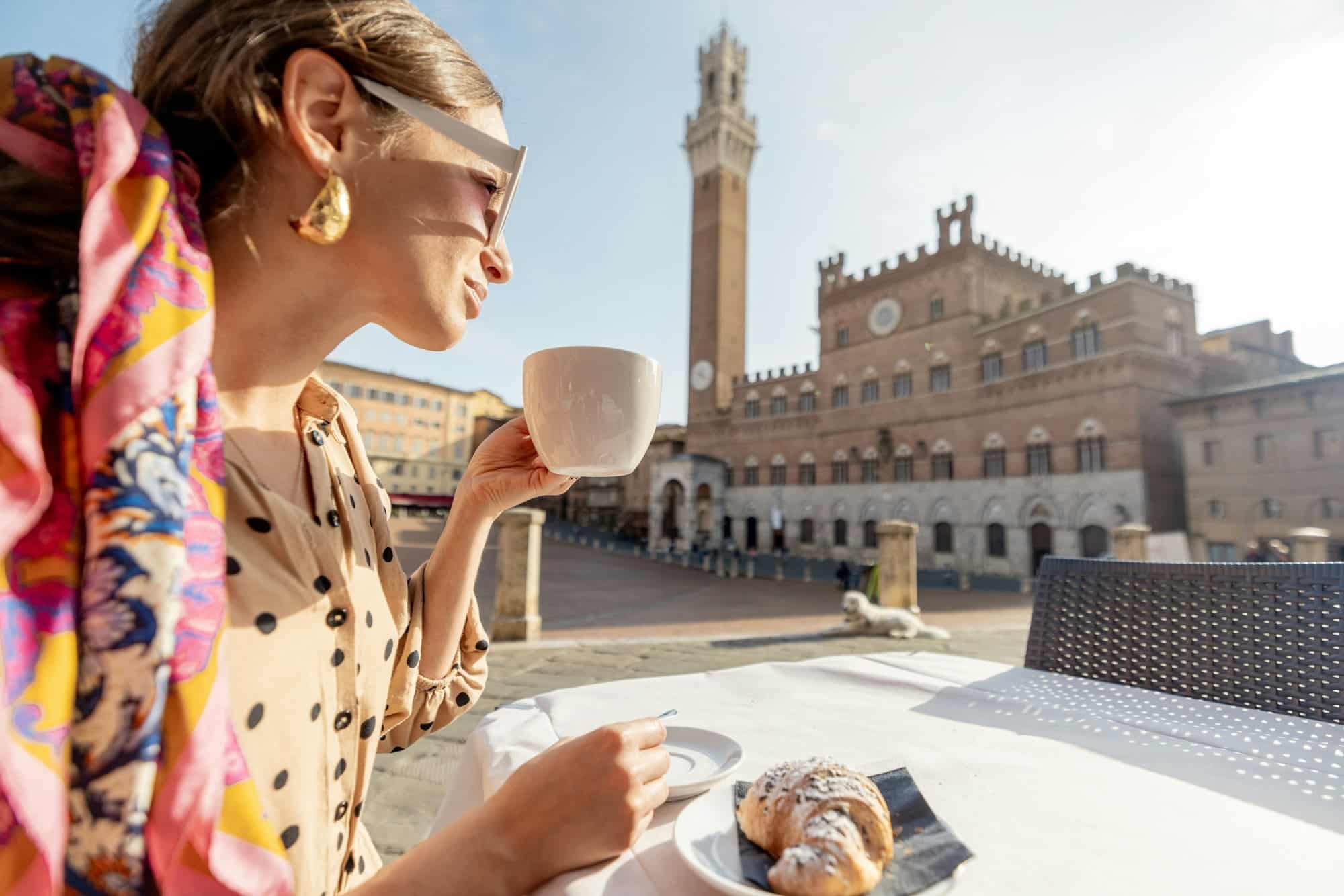 Woman having breakfast at outdoor cafe with beautiful view on main square of Siena city, Italy