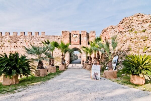 Rocca medievale con palme e percorso in ghiaia.