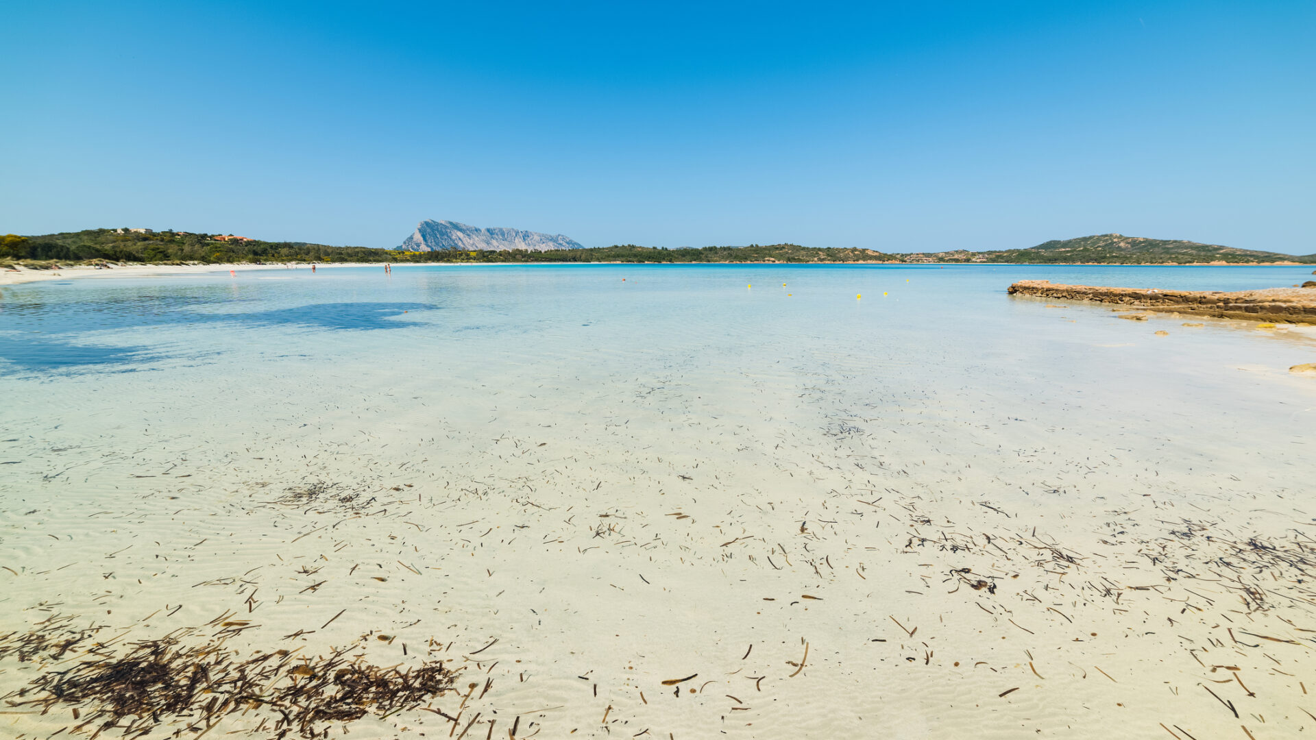 Spiaggia sarda con acqua cristallina e montagne.
