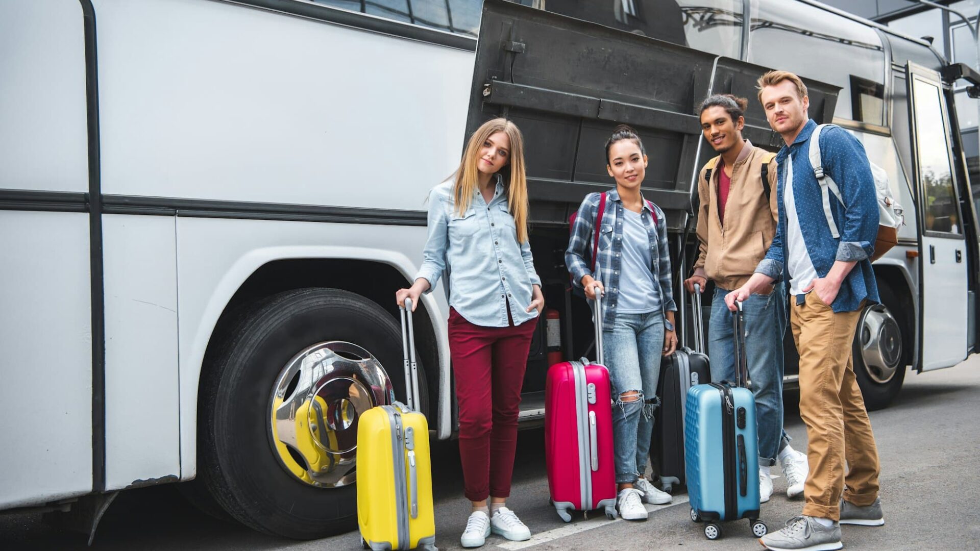 amigos multiculturales con bolsas de viaje posando cerca de autobús de viaje en la calle