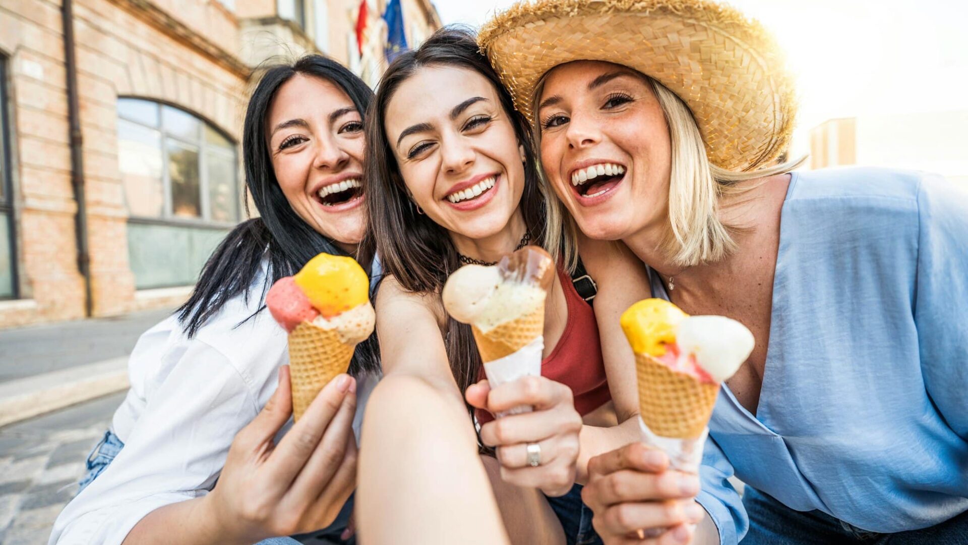 Three cheerful teenage women eating ice cream cones on city street