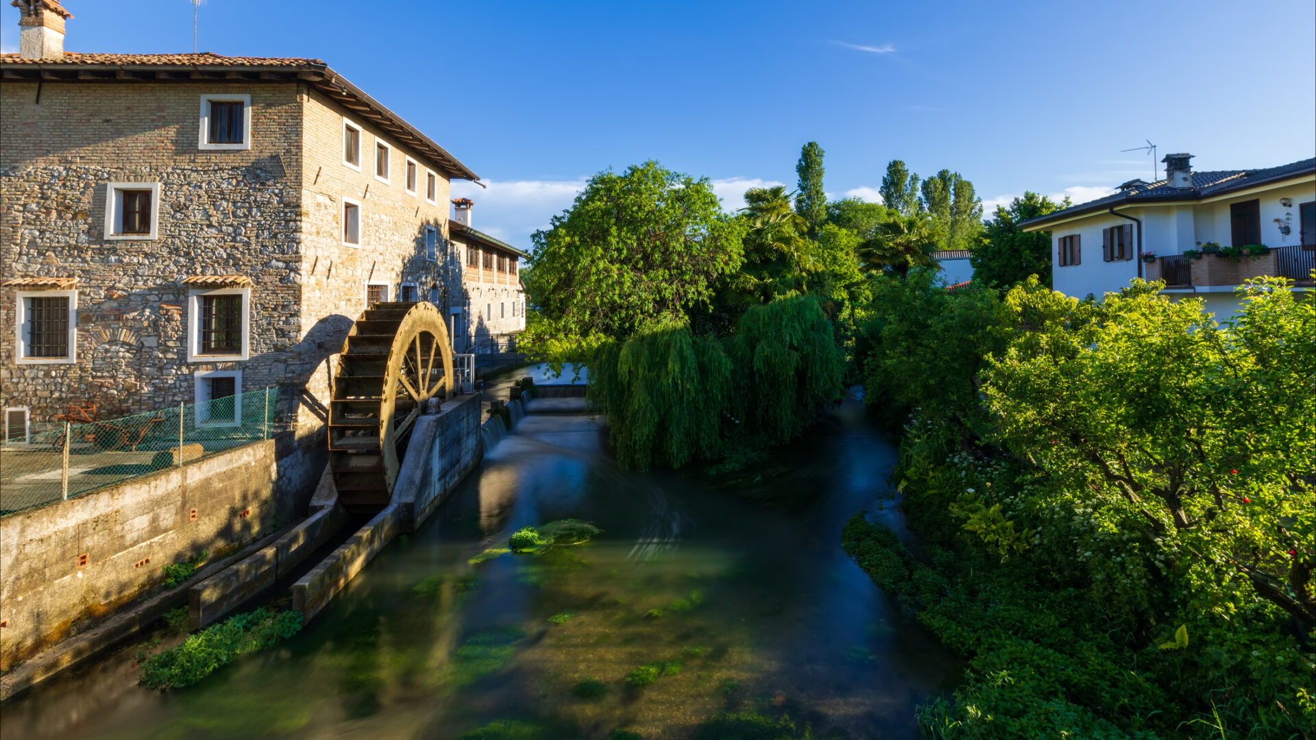 Antico mulino a pale sul fiume nel borgo medievale di Strassoldo. Italia. Uno dei borghi più belli d'Italia. Vegetazione spontanea.
