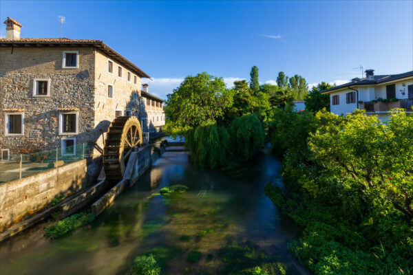 Antico mulino a pale sul fiume nel borgo medievale di Strassoldo. Italia. Uno dei borghi più belli d'Italia. Vegetazione spontanea.
