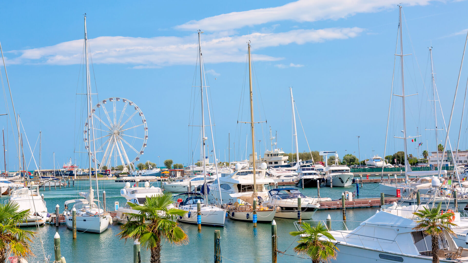 Vista estiva del molo con navi, yacht e altre barche con ruota panoramica a Rimini, Italia.