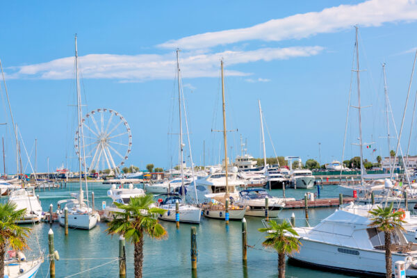 Vista estiva del molo con navi, yacht e altre barche con ruota panoramica a Rimini, Italia.