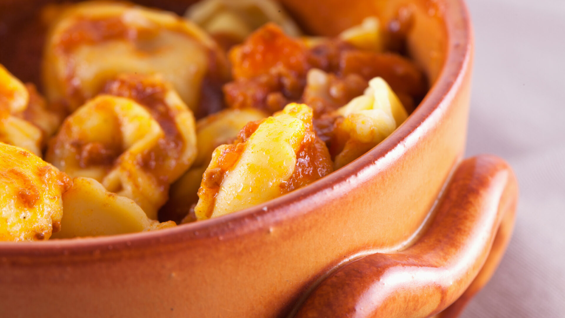 Agnolotti with tomato sauce in an earthenware pot, close-up