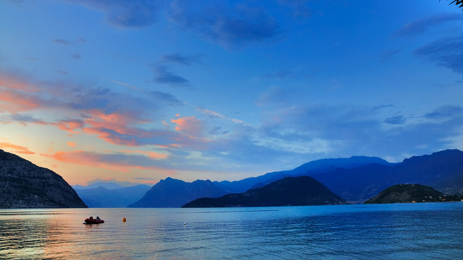 Tramonto sul lago con barca e montagne.