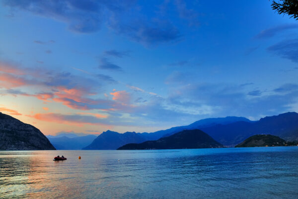 Sunset over the lake with boat and mountains.