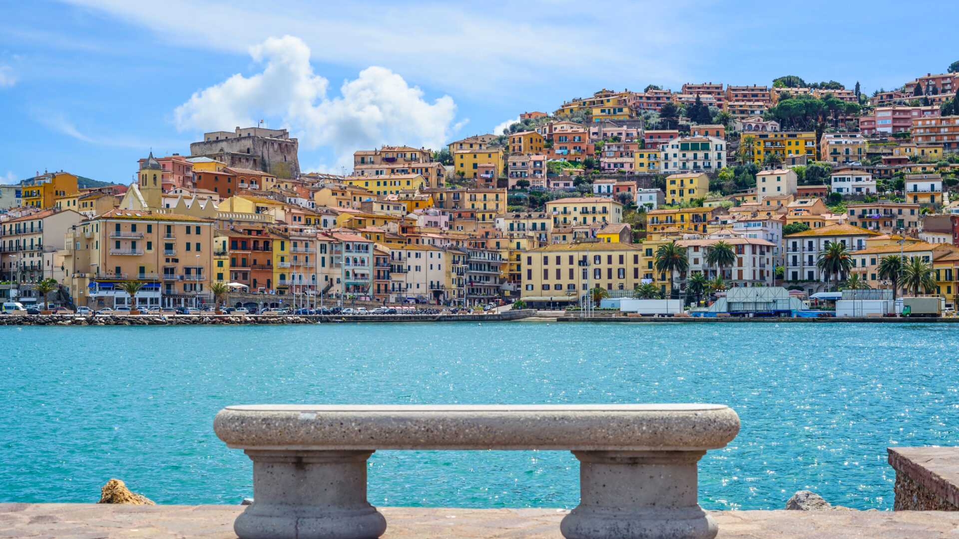 长椅面朝大海，背景是色彩斑斓的房屋。