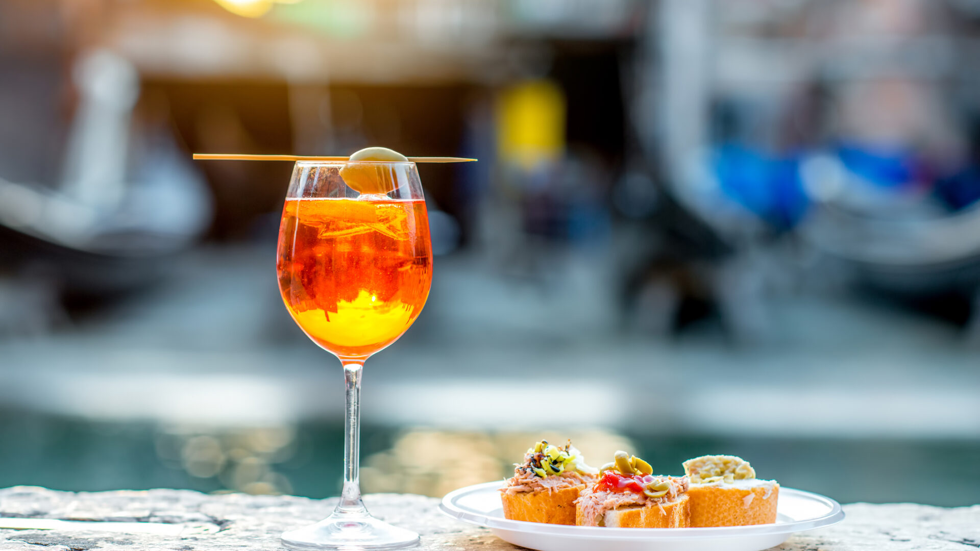 Spritz Aperol con cicchetti. Spritz Aperol con cicchetti sulla sfondo dell'acqua a Venezia. Aperitivo tradizionale italiano. Immagine con piccola profondità di campo