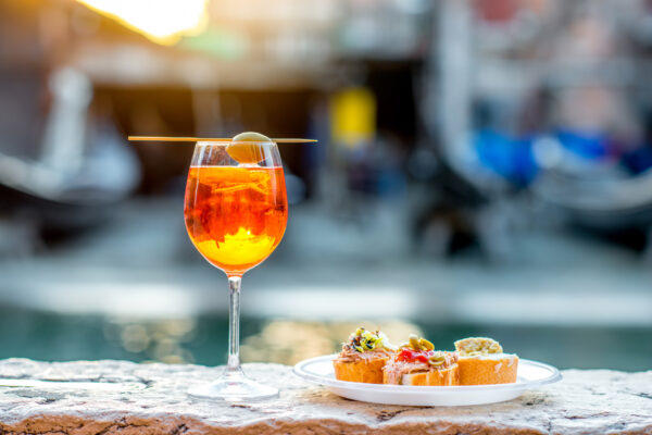 Spritz Aperol con cicchetti. Spritz Aperol con cicchetti con el agua como telón de fondo en Venecia. Aperitivo tradicional italiano. Imagen con poca profundidad de campo