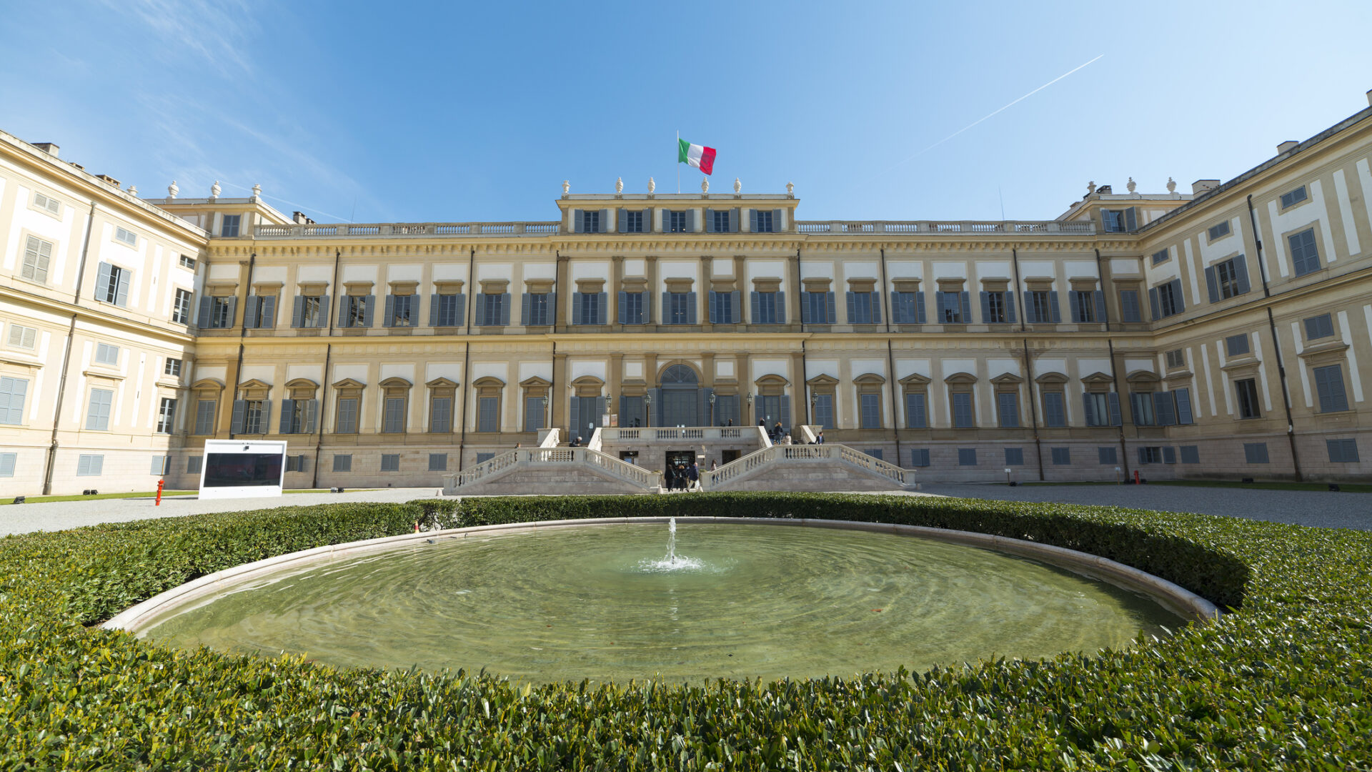 Reggia storica con fontana centrale e bandiera italiana.