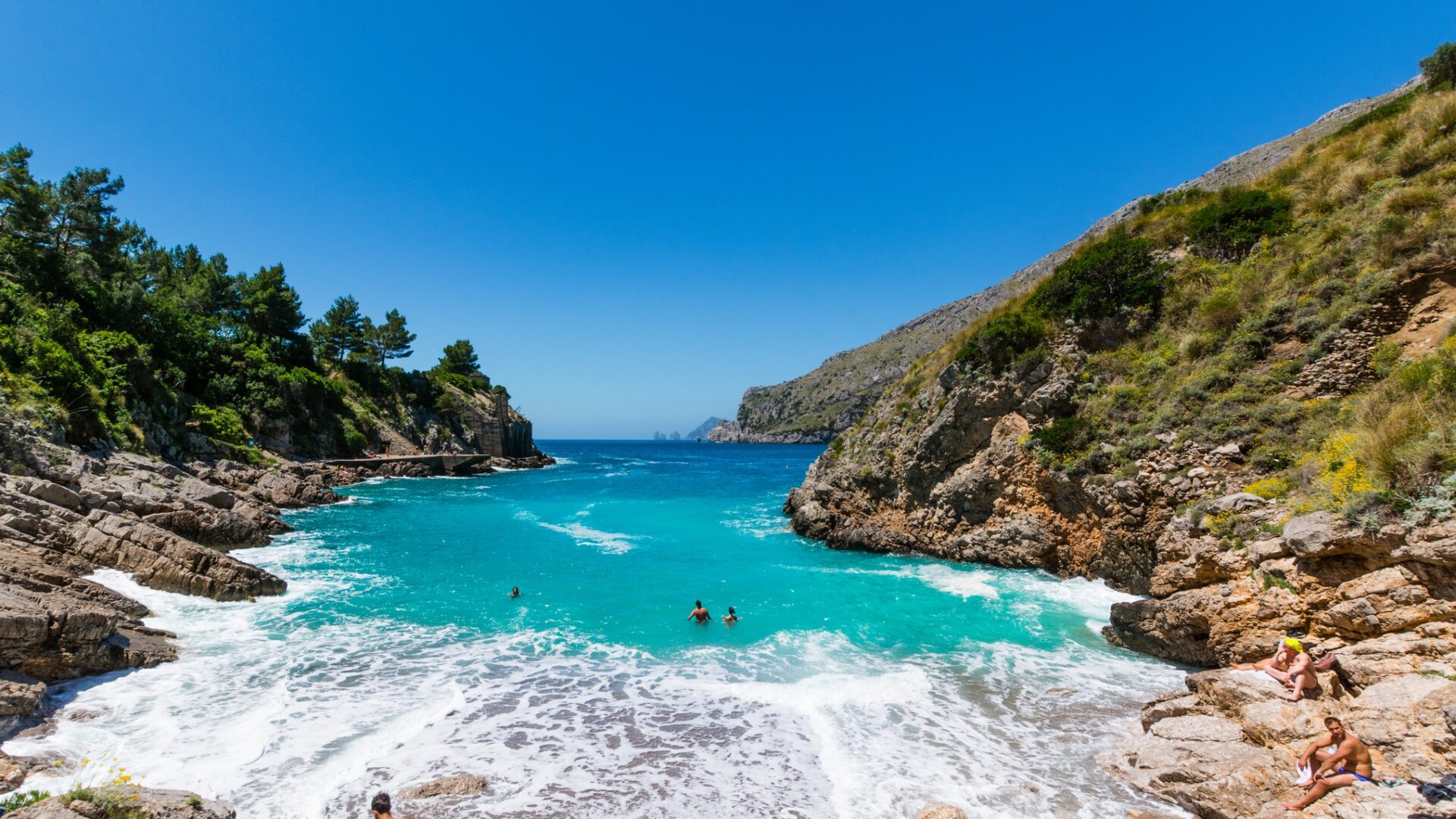 Caletta rocciosa con acqua cristallina e persone nuotando