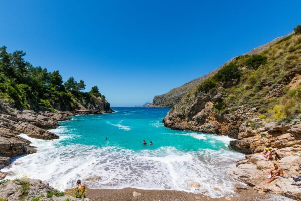 Caletta rocciosa con acqua cristallina e persone nuotando