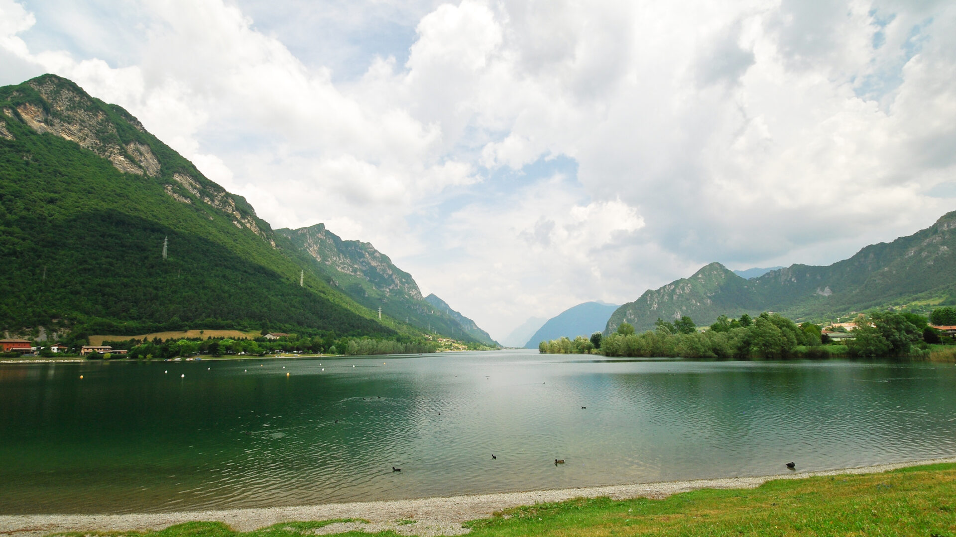 Lac clair entouré de montagnes vertes et d'un ciel nuageux