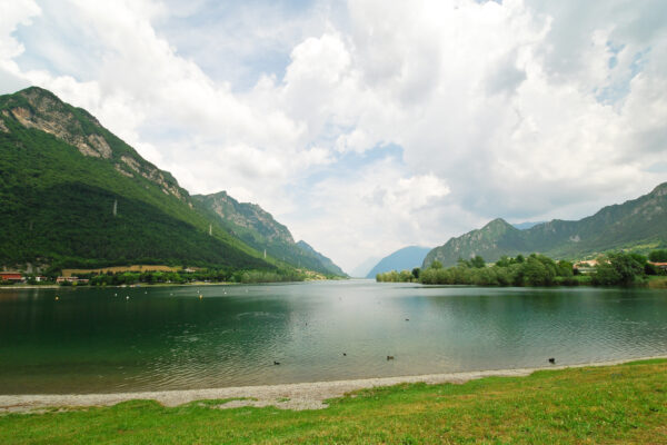 Lago claro rodeado de montañas verdes y cielos nublados
