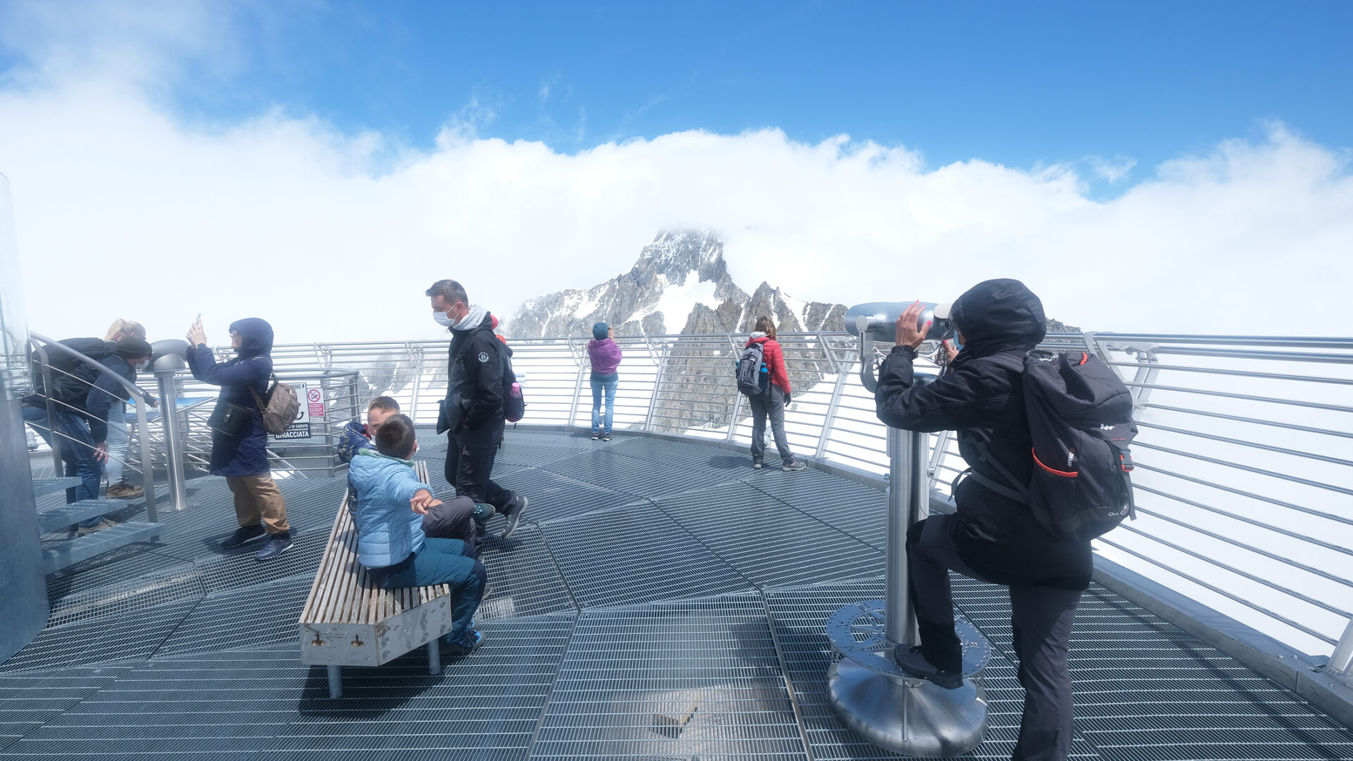 Turisti osservano montagne nevose da piattaforma panoramica