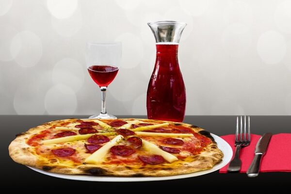 Pizza con salame e ananas, vino rosso in caraffa.