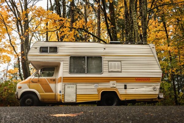 Camper vintage su strada autunnale con alberi.