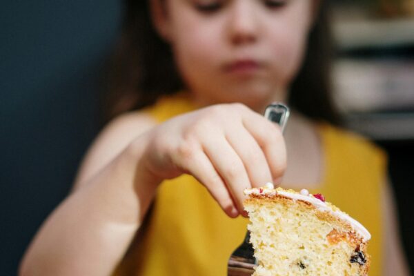 Bambina con fetta di torta su piatto giallo.