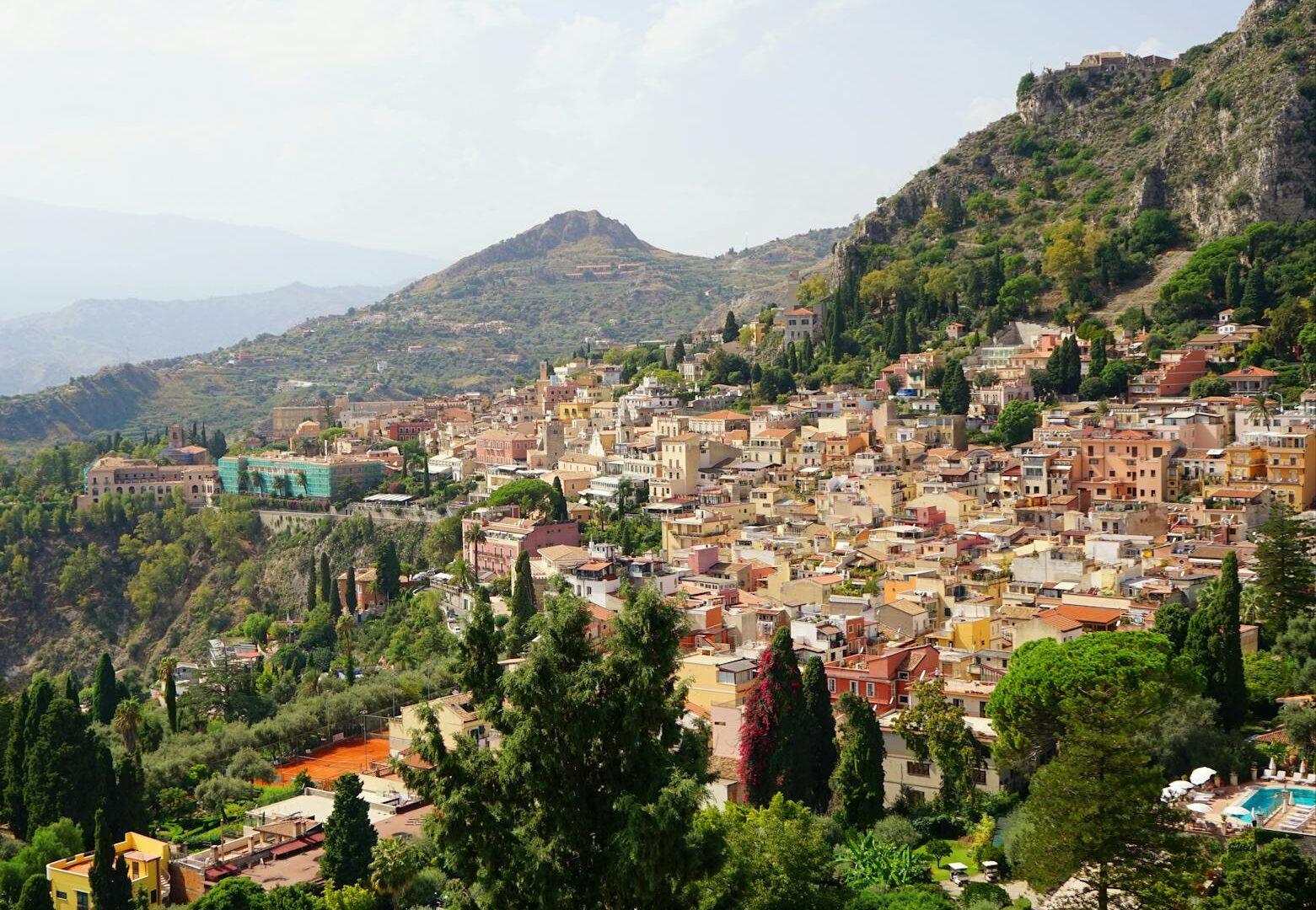 Vista panoramica di Taormina, colline verdi, case colorate.