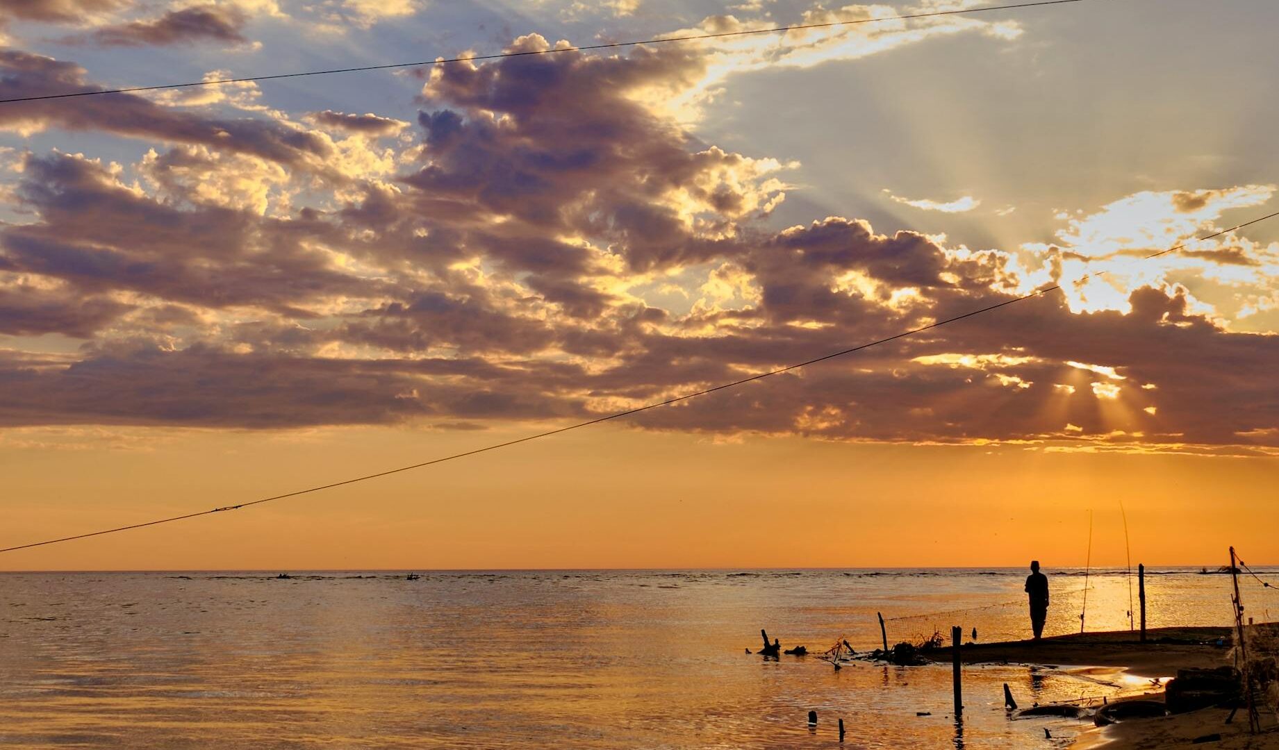 Tramonto su una spiaggia con pescatore solitario