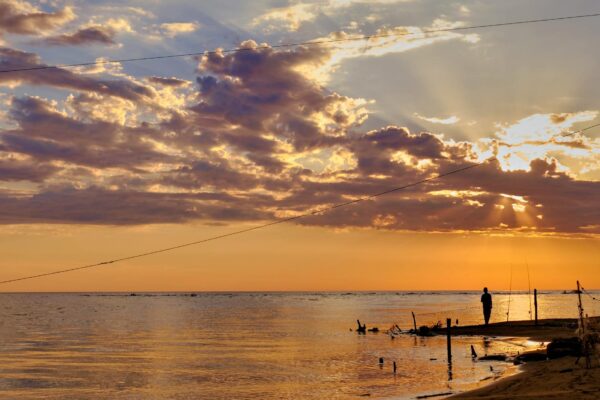 Tramonto su una spiaggia con pescatore solitario