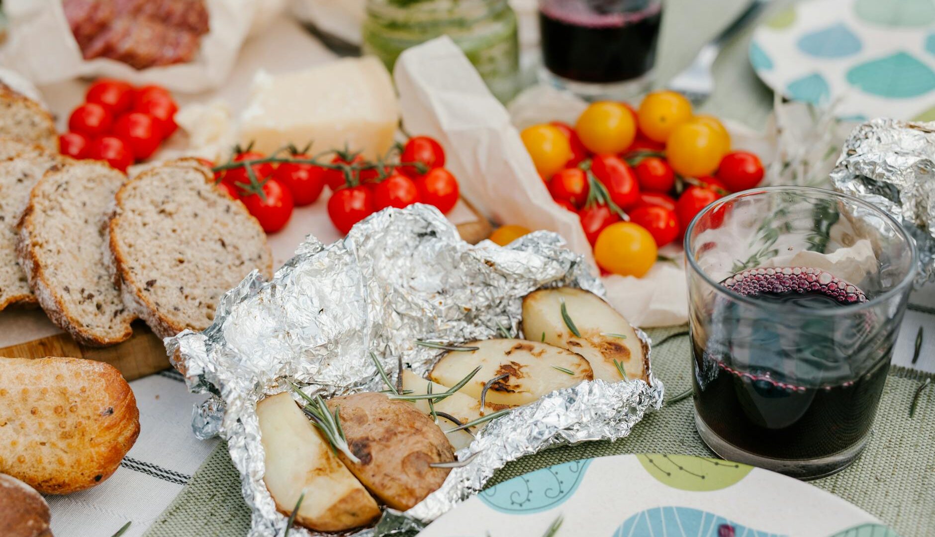 Picnic con pane, pomodori, patate e vino rosso.