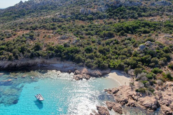 Spiaggia con barca in mare turchese e vegetazione.