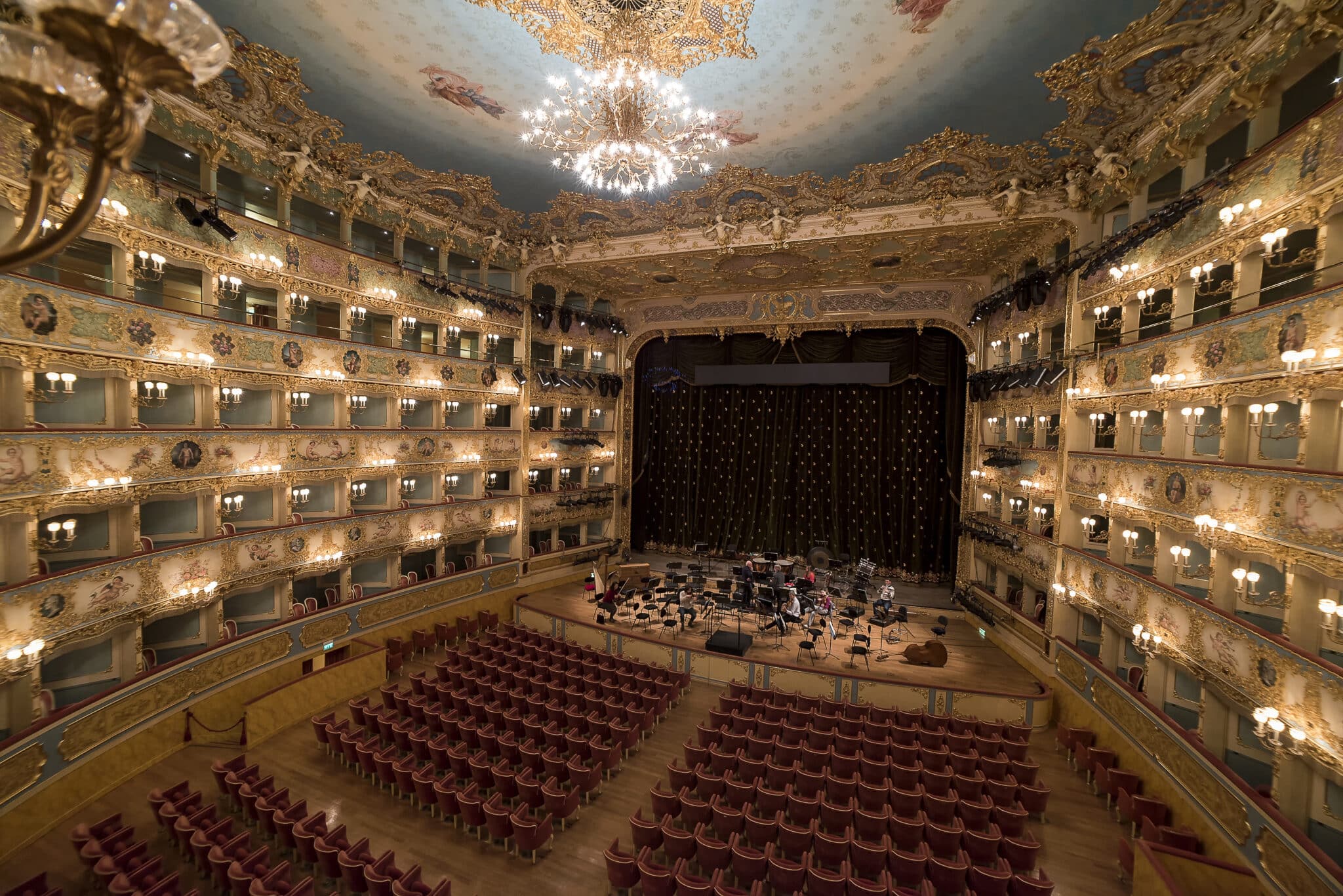 Teatro storico vuoto con palchetti dorati e lampadario.