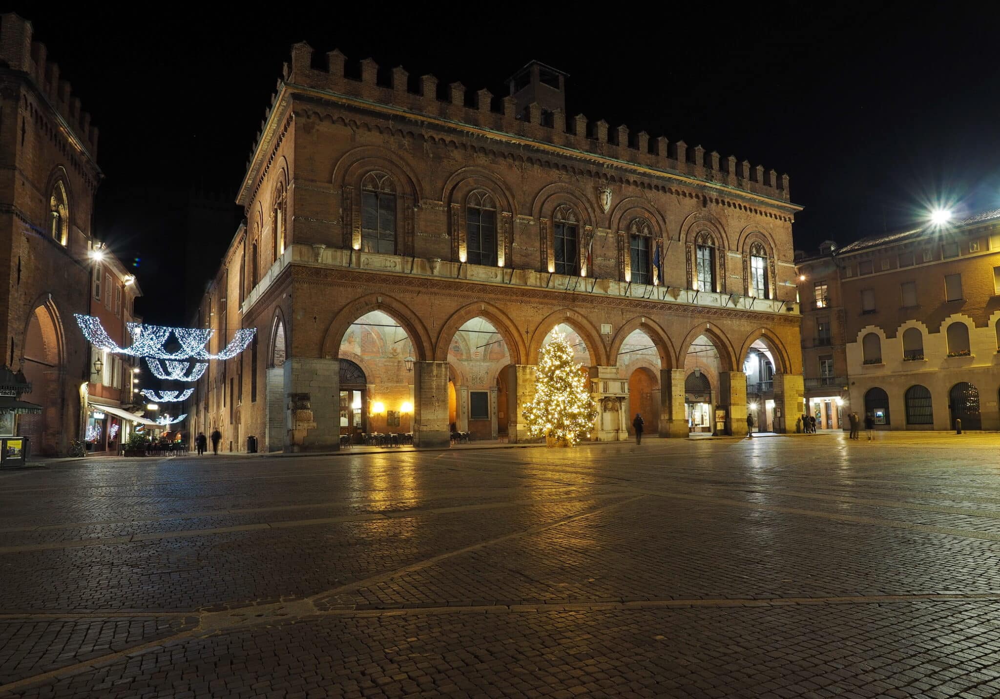 Piazza illuminata con edifici storici e decorazioni natalizie.