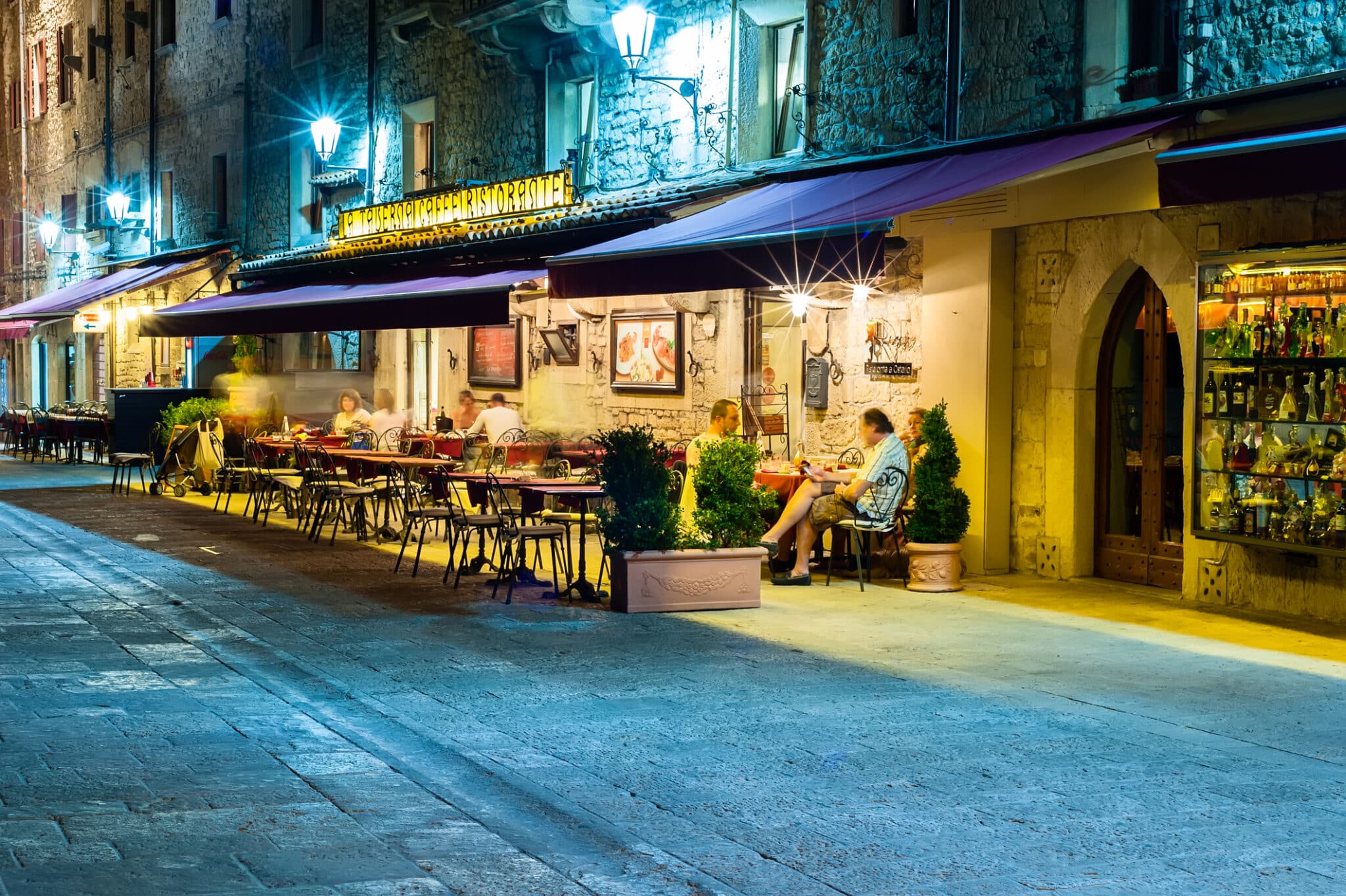 Vita notturna sammarinese. Persone in un caffè sul marciapiede sulla strada di San Marino, godendosi l'estate e sorseggiando un drink.