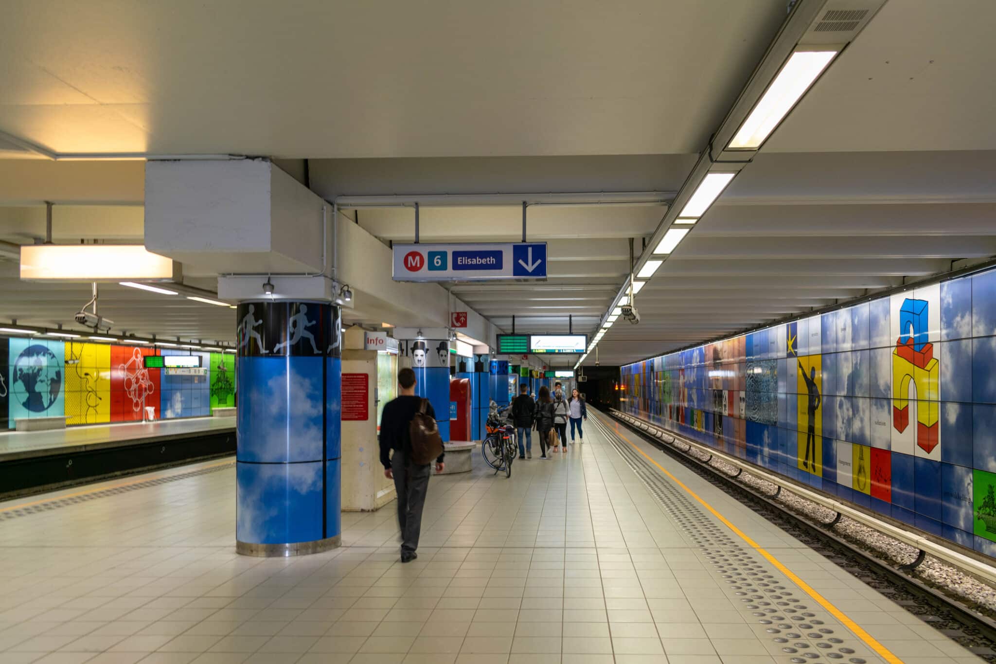 Stazione metro artistica con passeggeri e segnaletica.