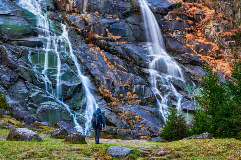 Randonneur devant une cascade de montagne.