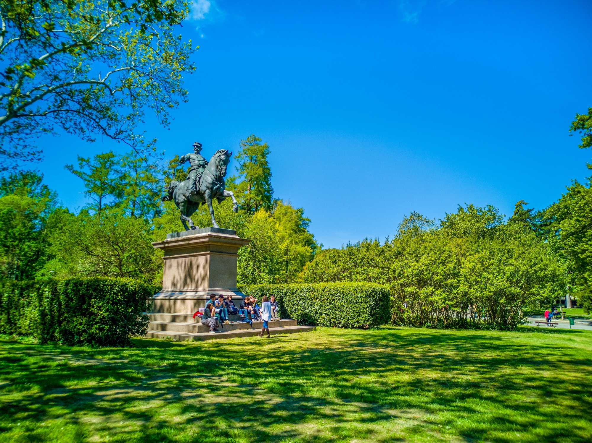 Statua equestre in parco soleggiato con persone.