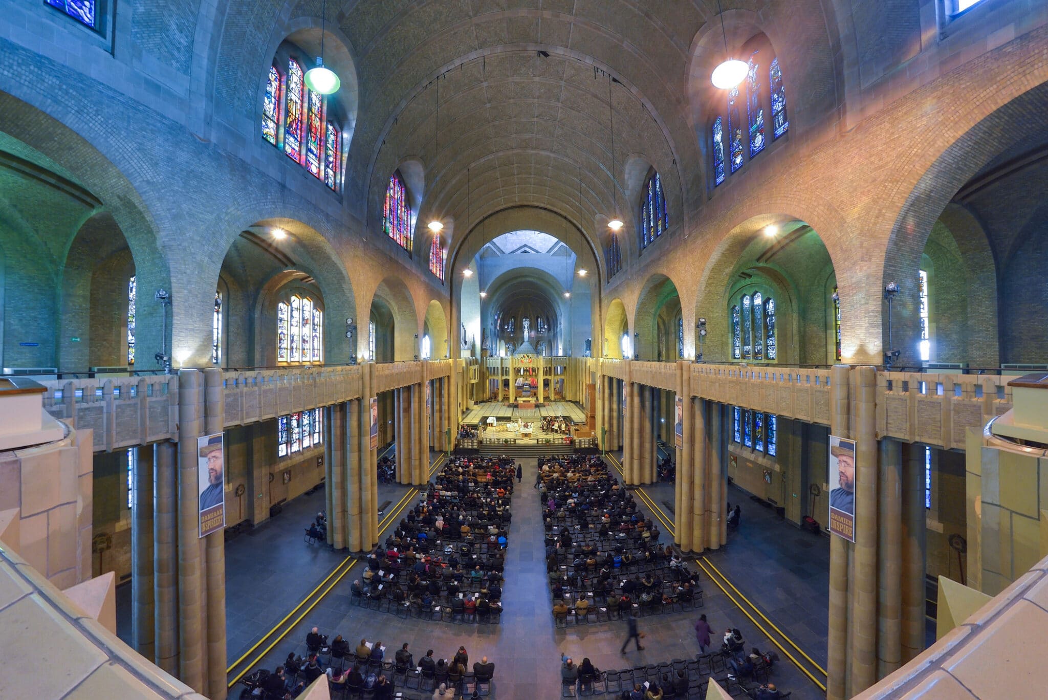 Interni chiesa gotica, vetrate colorate, fedeli seduti.