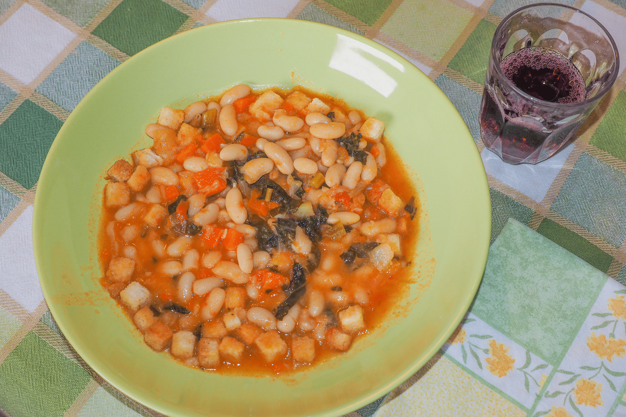 Piatto di Ribollita Toscana in una ciotola verde, servito con un bicchiere di vino rosso.