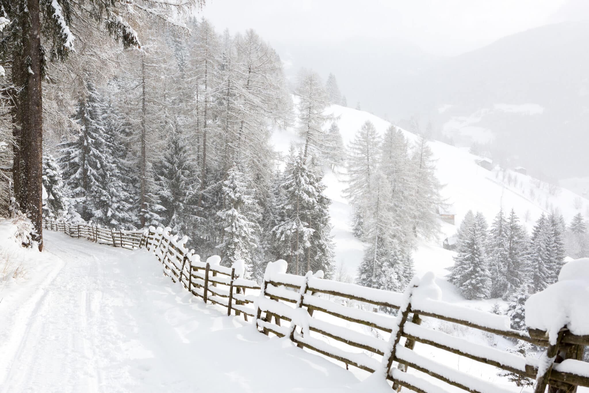 Strada di campagna tortuosa in discesa con vista panoramica sulle montagne durante la nevicata vicino a Vipiteno Alto Adige, Dolomiti, Italia settentrionale