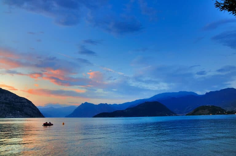 夕阳西下，湖面上有小船和群山。