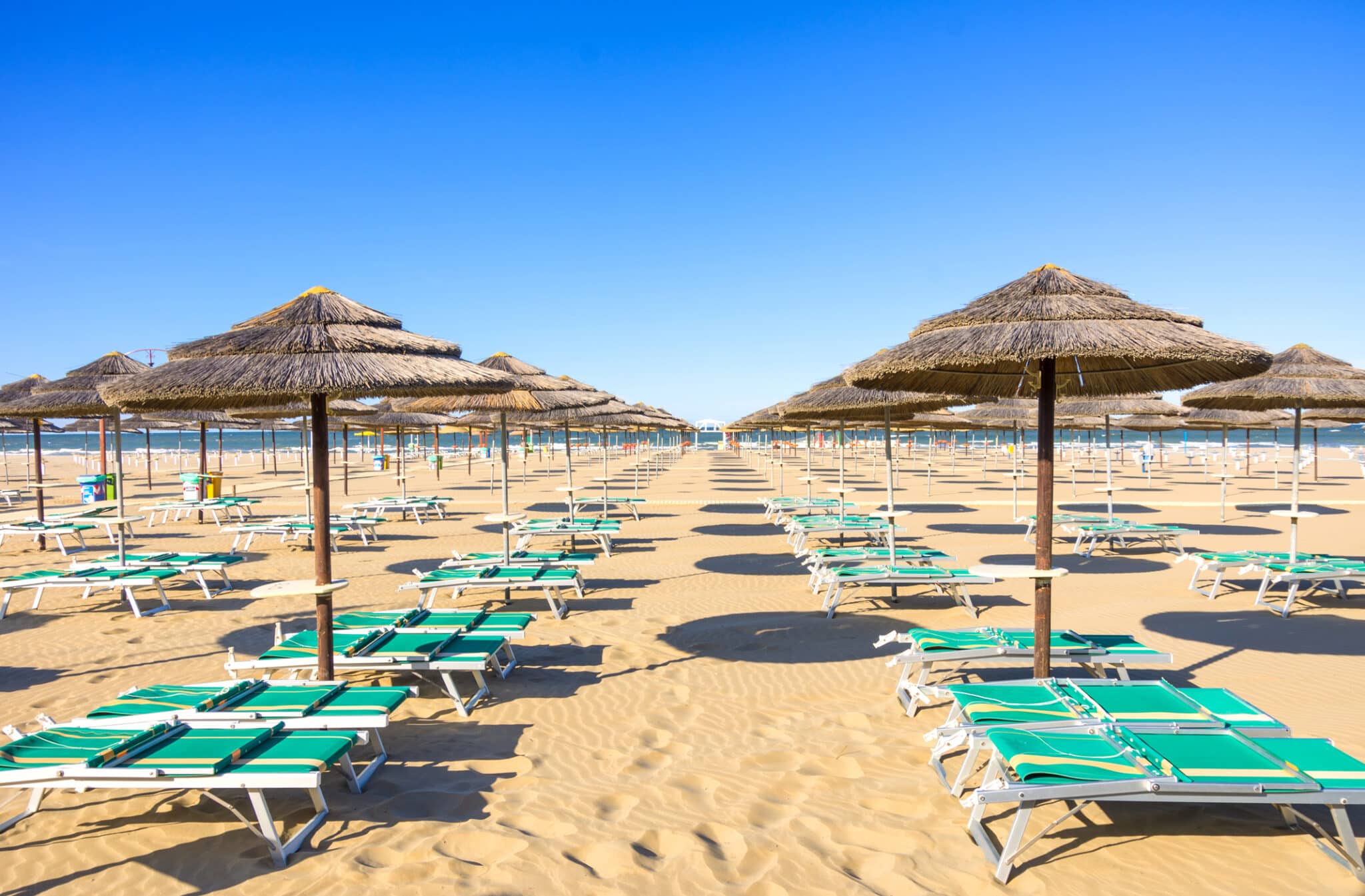 Spiaggia sabbiosa con ombrelloni e lettini al sole.