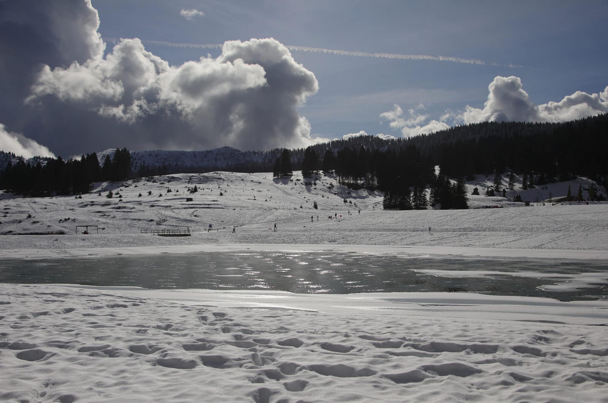 lago di montagna ghiacciato in inverno con neve bianca e nuvole bianche in controluce