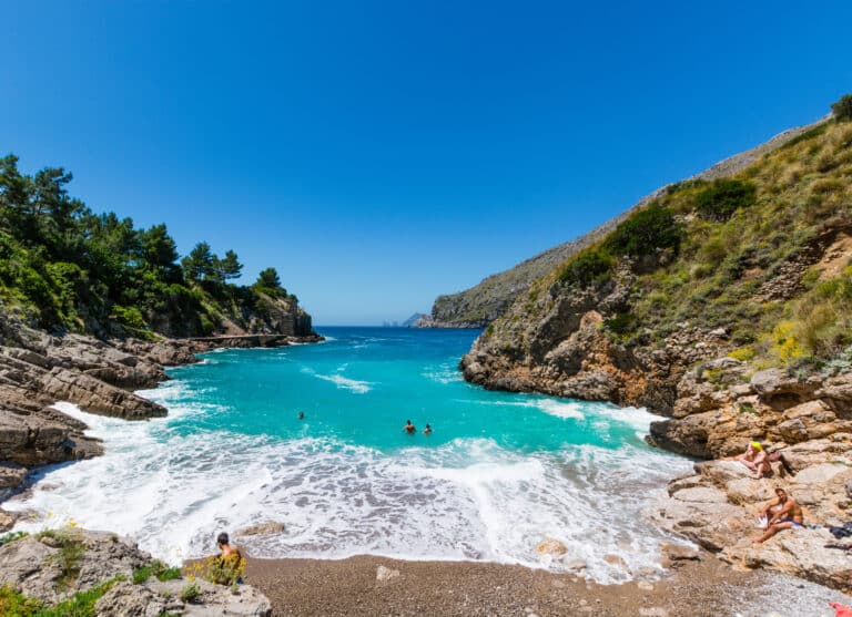Crique rocheuse avec une eau cristalline et des gens qui se baignent